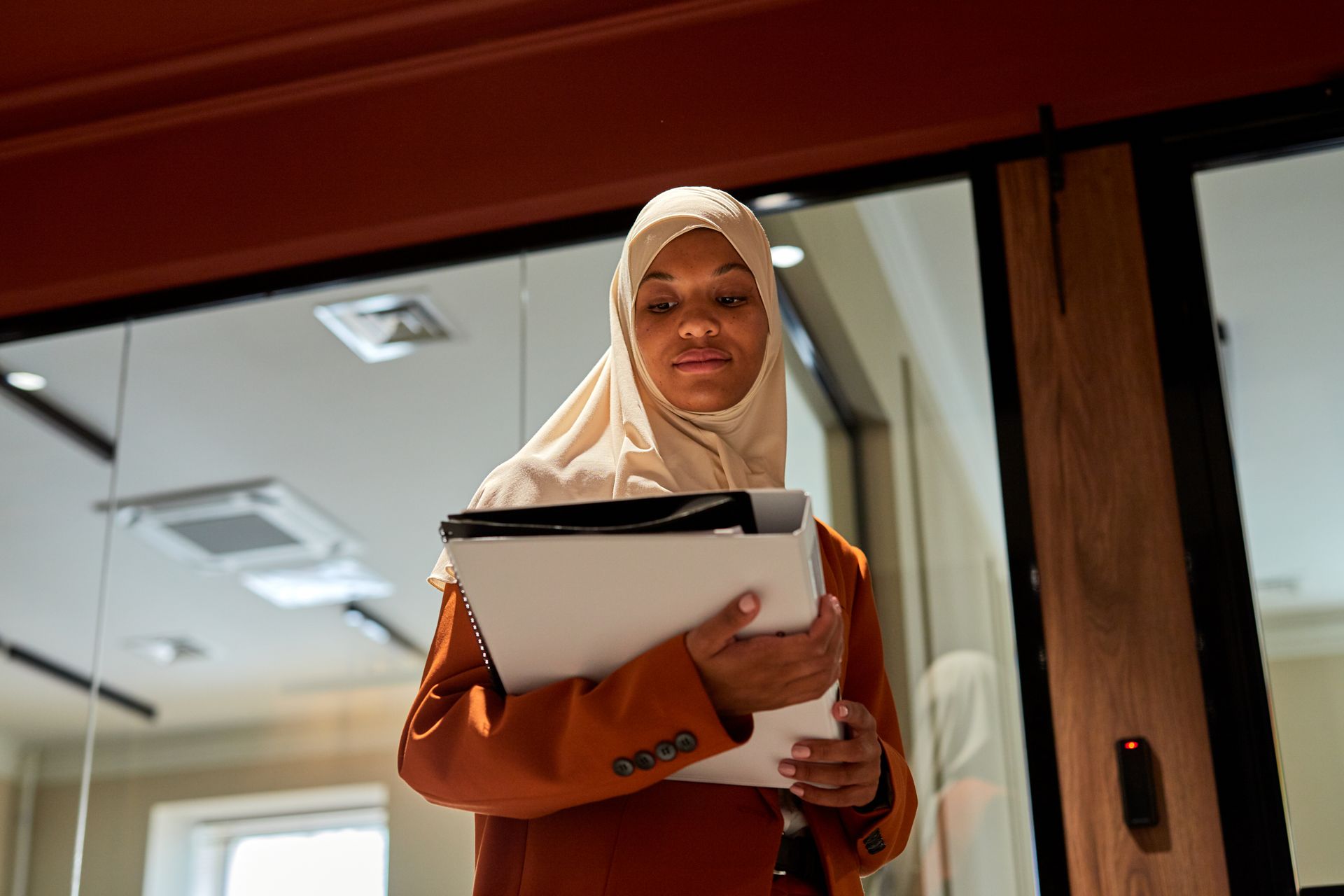 A Black businesswoman in a hijab holding a laptop in a corporate office