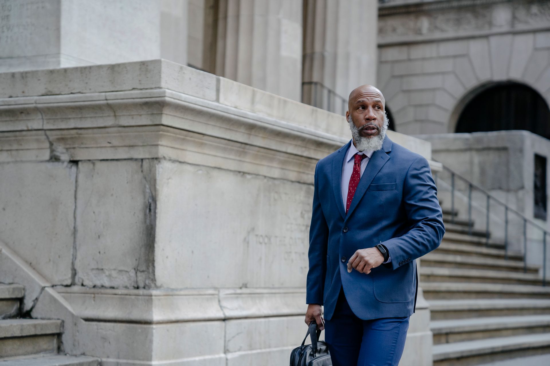 A Black executive in a business suit walking past an institutional building