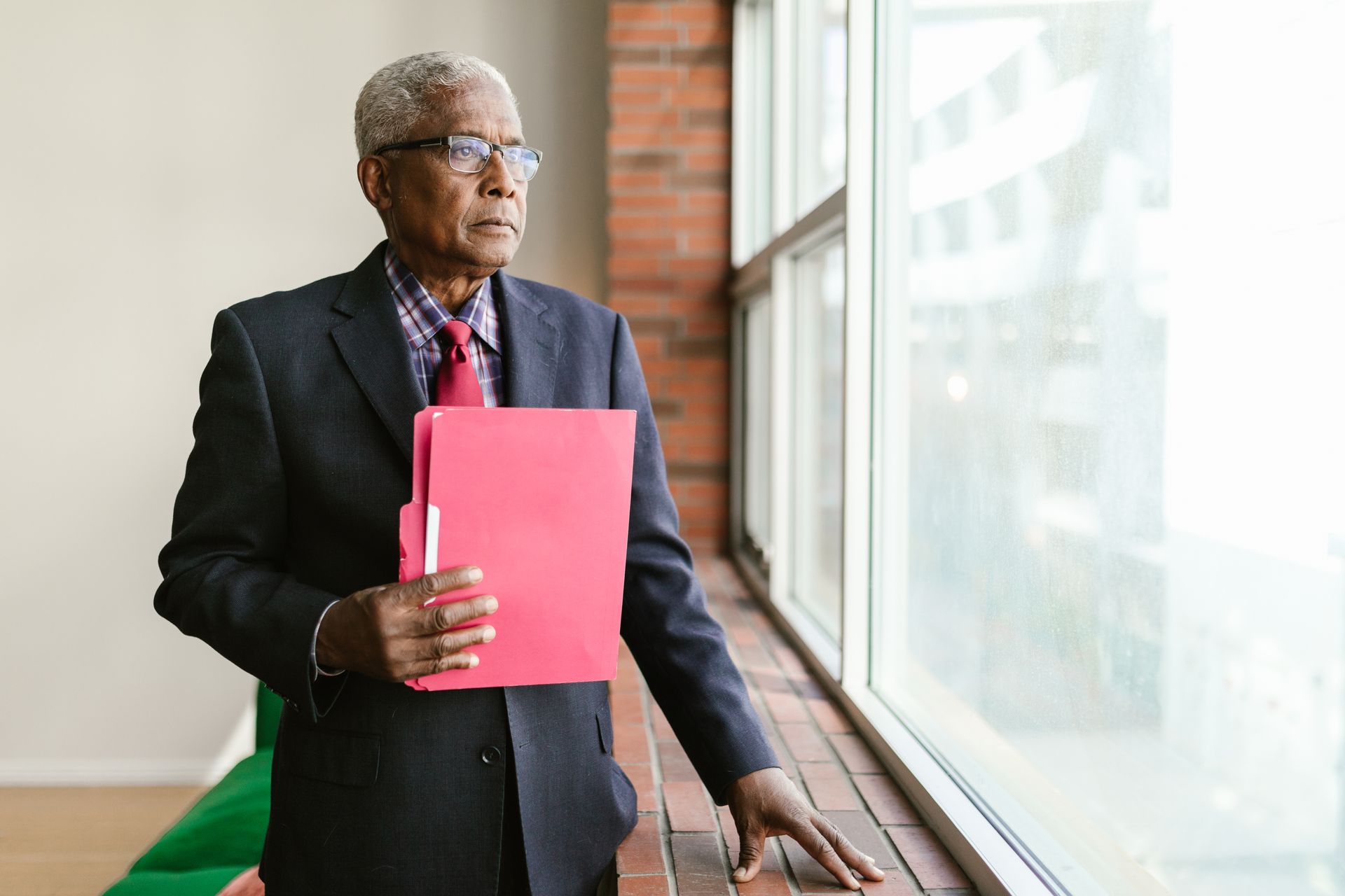 A senior Black executive in a suit holding a folder beside an office window