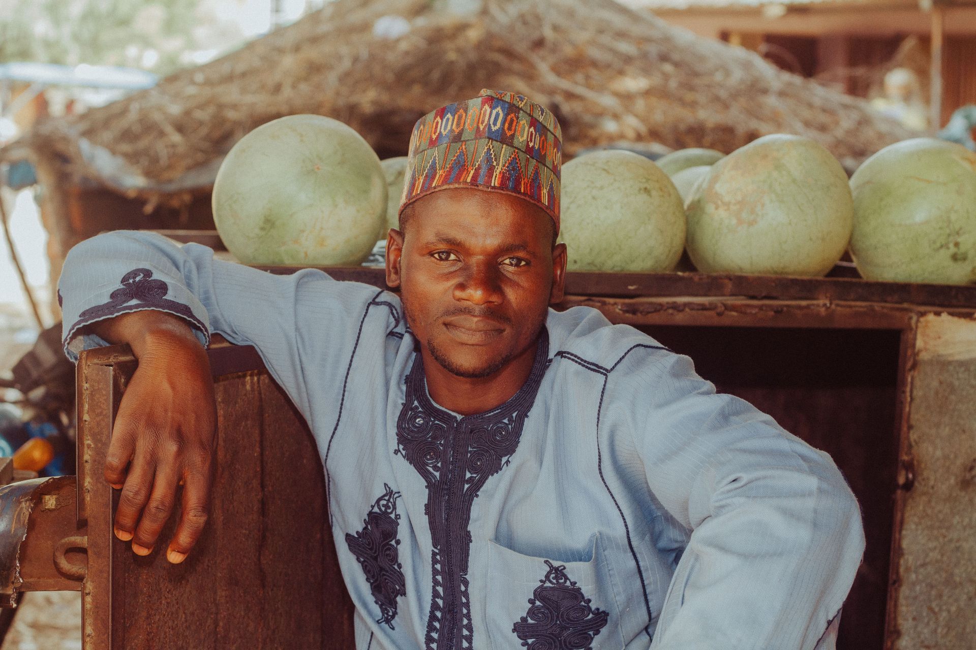 A young Nigerian man in a traditional cap beside his melon stall in Zaria