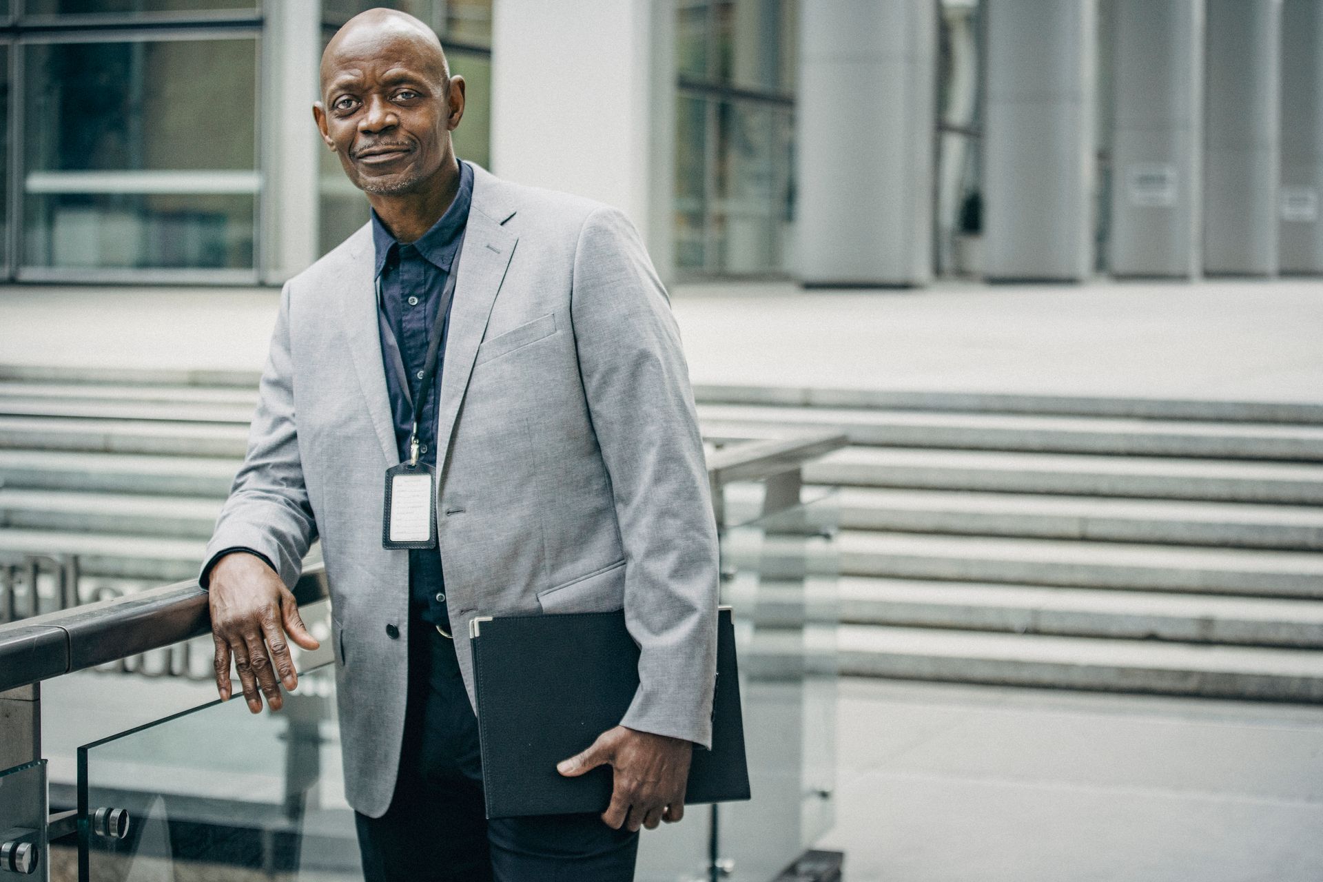 A Black professional in a suit and staff badge outside a modern office building