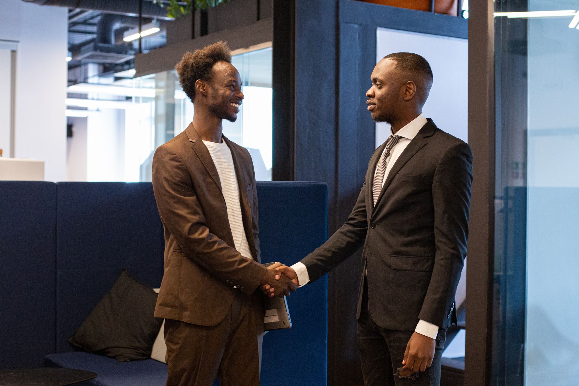 Two Black business professionals in suits shaking hands in a modern office